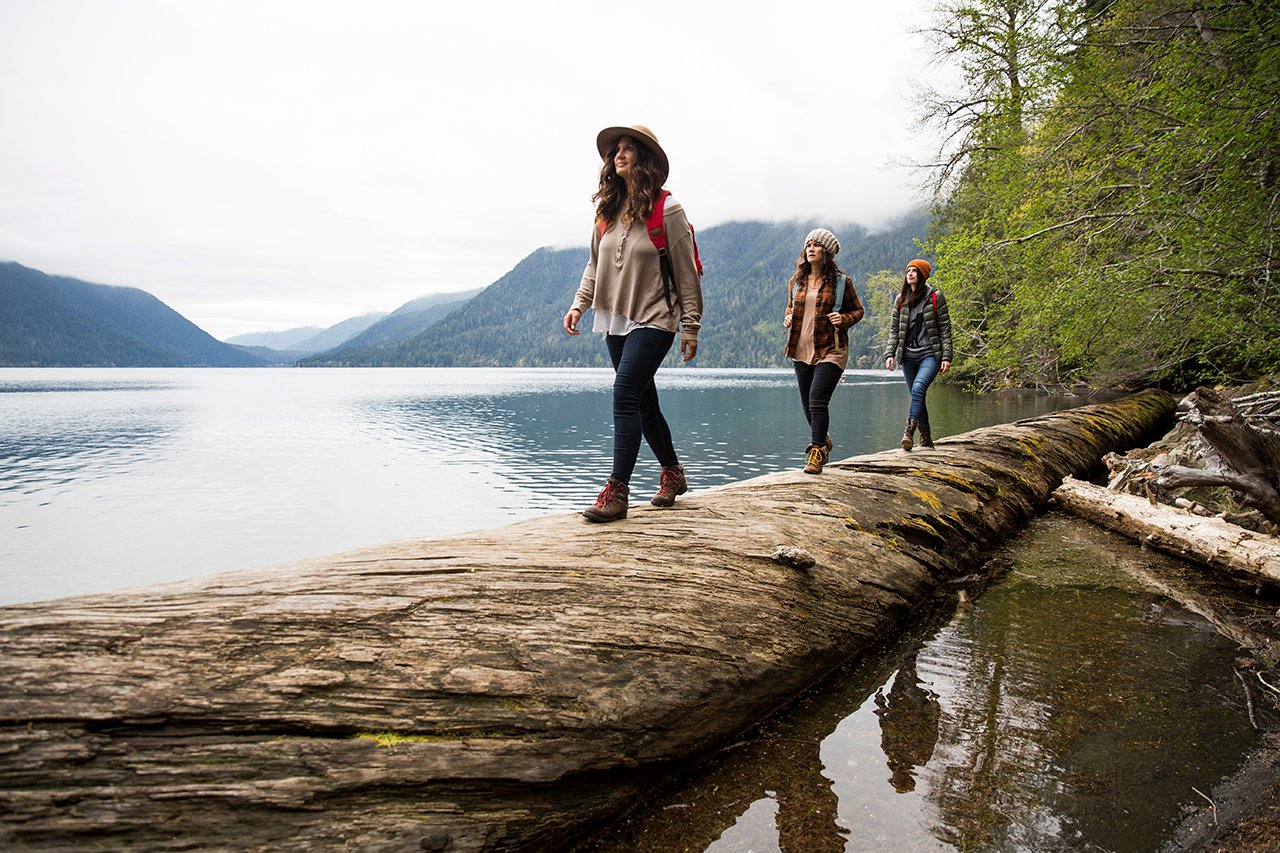 Hikers walking across log at lake